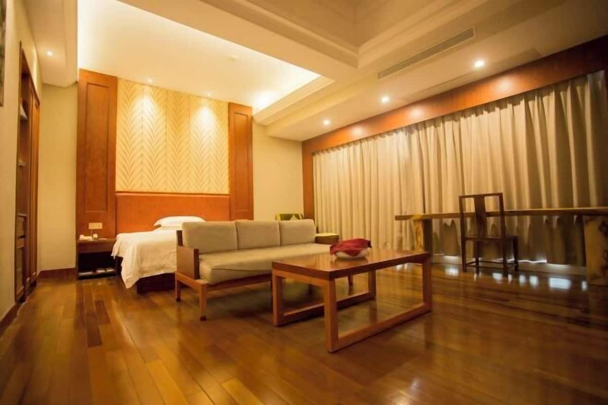 Habitación de hotel con cama, sofá, mesita de centro de madera y zona de comedor con mesa y sillas.