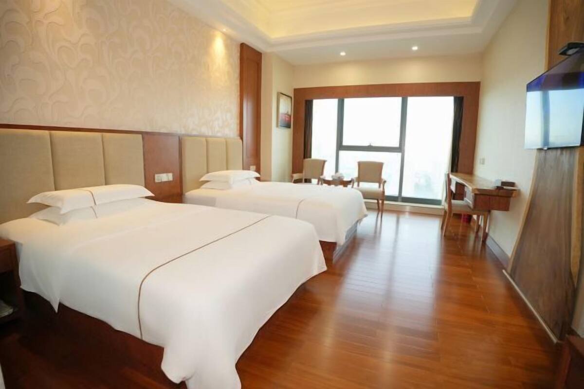 Una habitación de hotel con dos camas, un escritorio, sillas y un ventanal grande.
