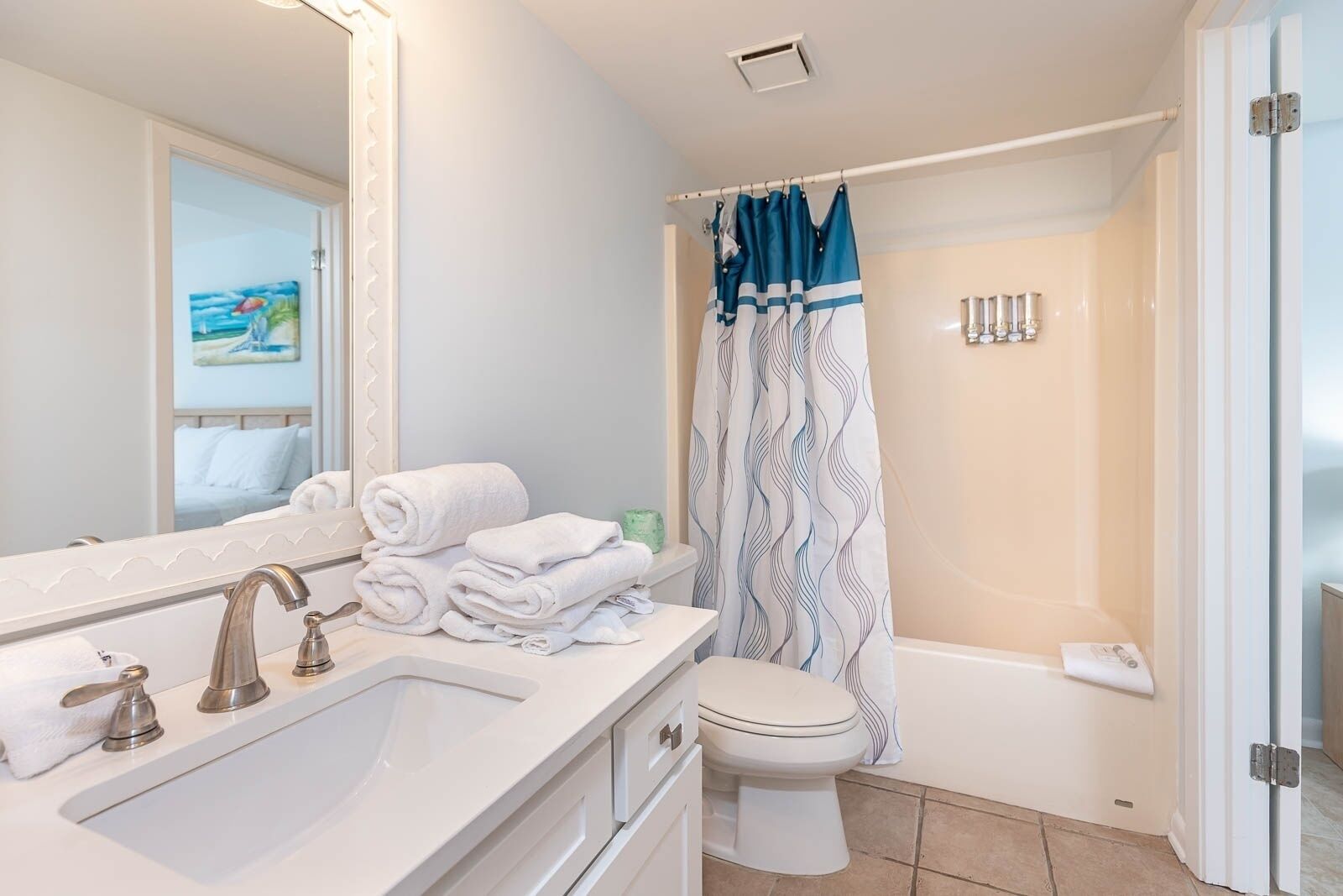 Une salle de bain moderne avec un lavabo blanc, un miroir et des toilettes. Des serviettes sont pliées sur le lavabo et un rideau de douche aux motifs bleus et blancs est installé.