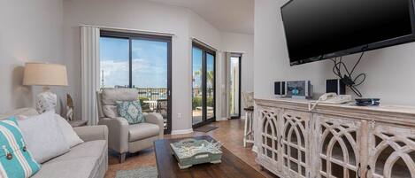A living room with a sofa, armchair, coffee table, and a TV mounted on the wall.