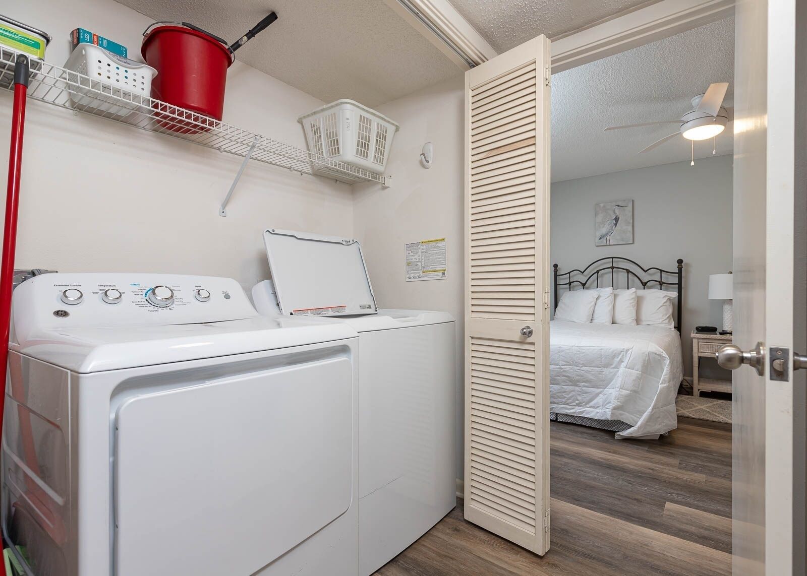Une petite pièce comprenant un lave-linge, un lit et une porte donnant sur une autre pièce.