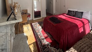 A bedroom with a bed, a mirror, a wardrobe, and a marble fireplace.