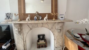 A marble fireplace with a mirror above it, a candelabra, and decorative items including a cat figurine and a chessboard.
