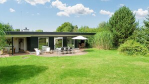 Una casa moderna con patio, mobiliario exterior y un gran árbol al fondo.