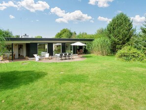 Ett modernt hus med en uteplats, utomhusmöbler och ett stort träd i bakgrunden.