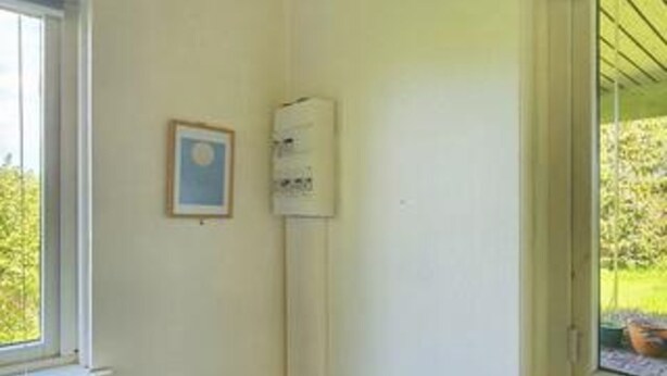 Una habitación con una ventana, un cuadro enmarcado y un dispositivo fijado a la pared.