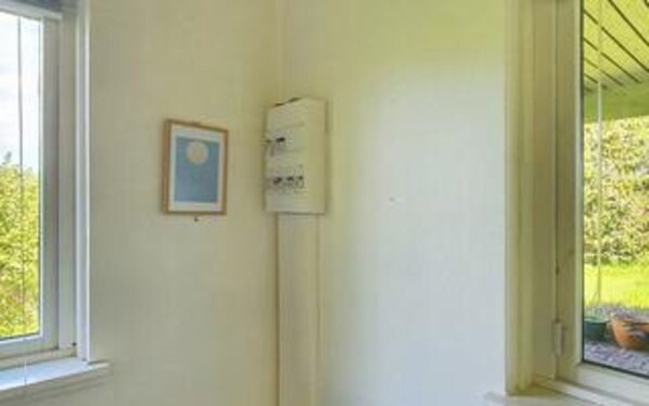 A room with a window, a framed picture, and a wall-mounted device.