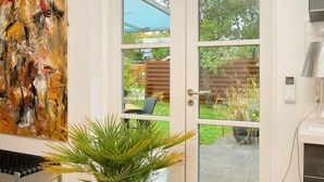 A room with a large abstract painting, a potted plant, and a view of a backyard through a glass door.