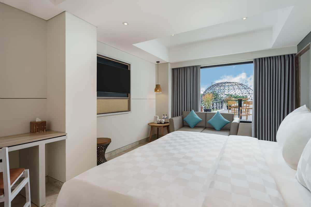A hotel room with a large bed, a desk, a small table, and a view of the outside.