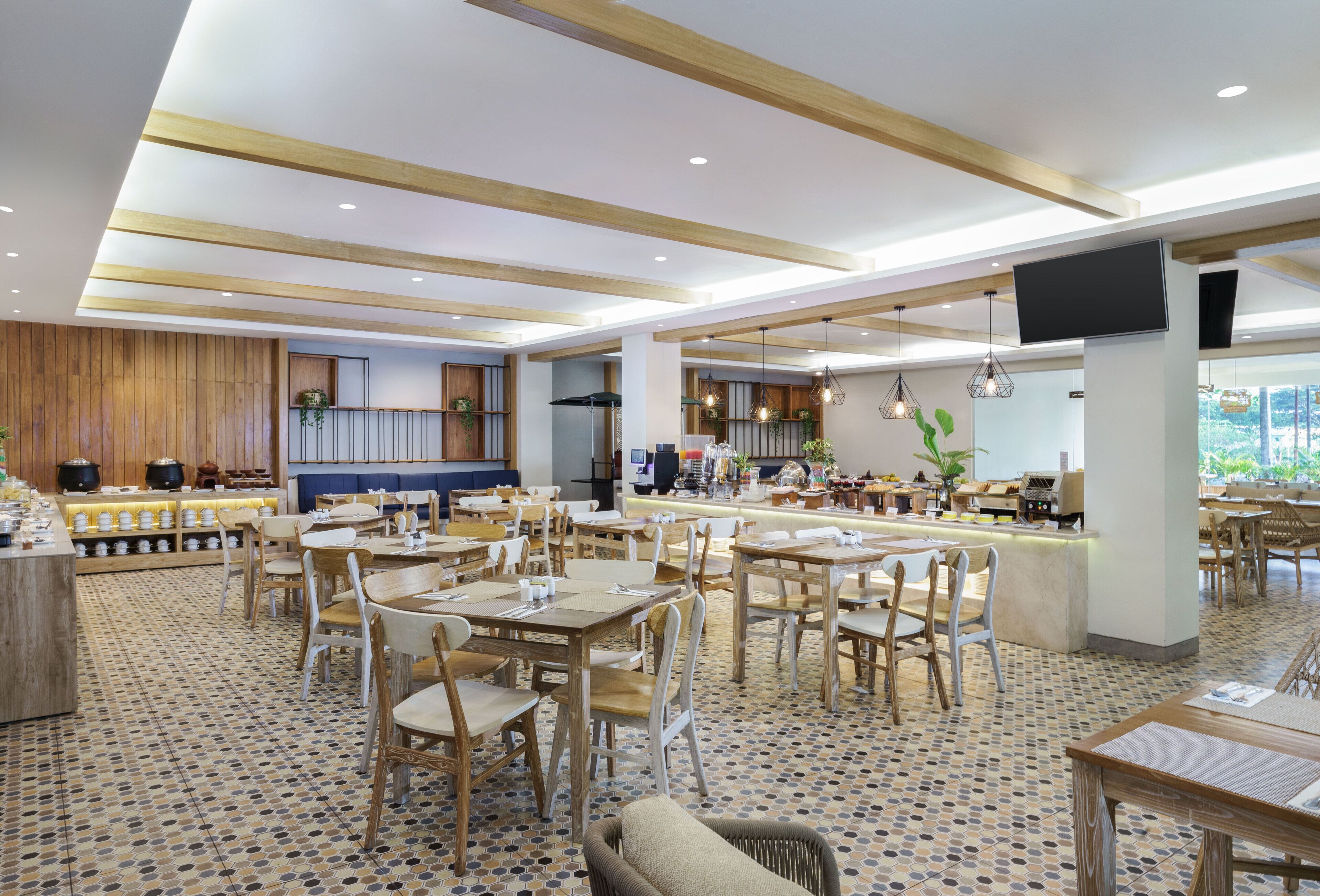 A spacious dining area with multiple tables and chairs, a kitchen area with modern appliances, and a large TV screen mounted on the wall.
