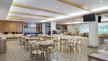 A spacious dining area with multiple tables and chairs, a kitchen area with modern appliances, and a large TV screen mounted on the wall.