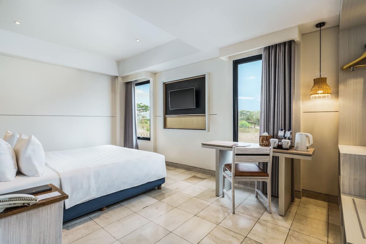 A hotel room with a bed, a desk, a chair, a television, and a window with curtains.