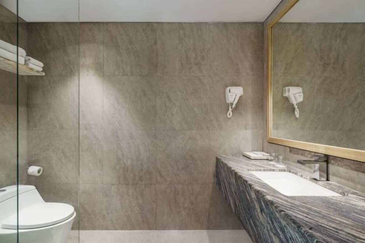 Un baño moderno con lavamanos de mármol, inodoro y un espejo grande.