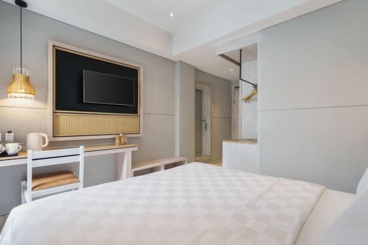Habitación de hotel moderna con una cama grande, un escritorio con una silla, un televisor montado en la pared y una lámpara colgante.