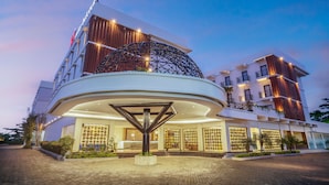 A modern hotel with a circular entrance, a prominent glass facade, and a rooftop terrace.