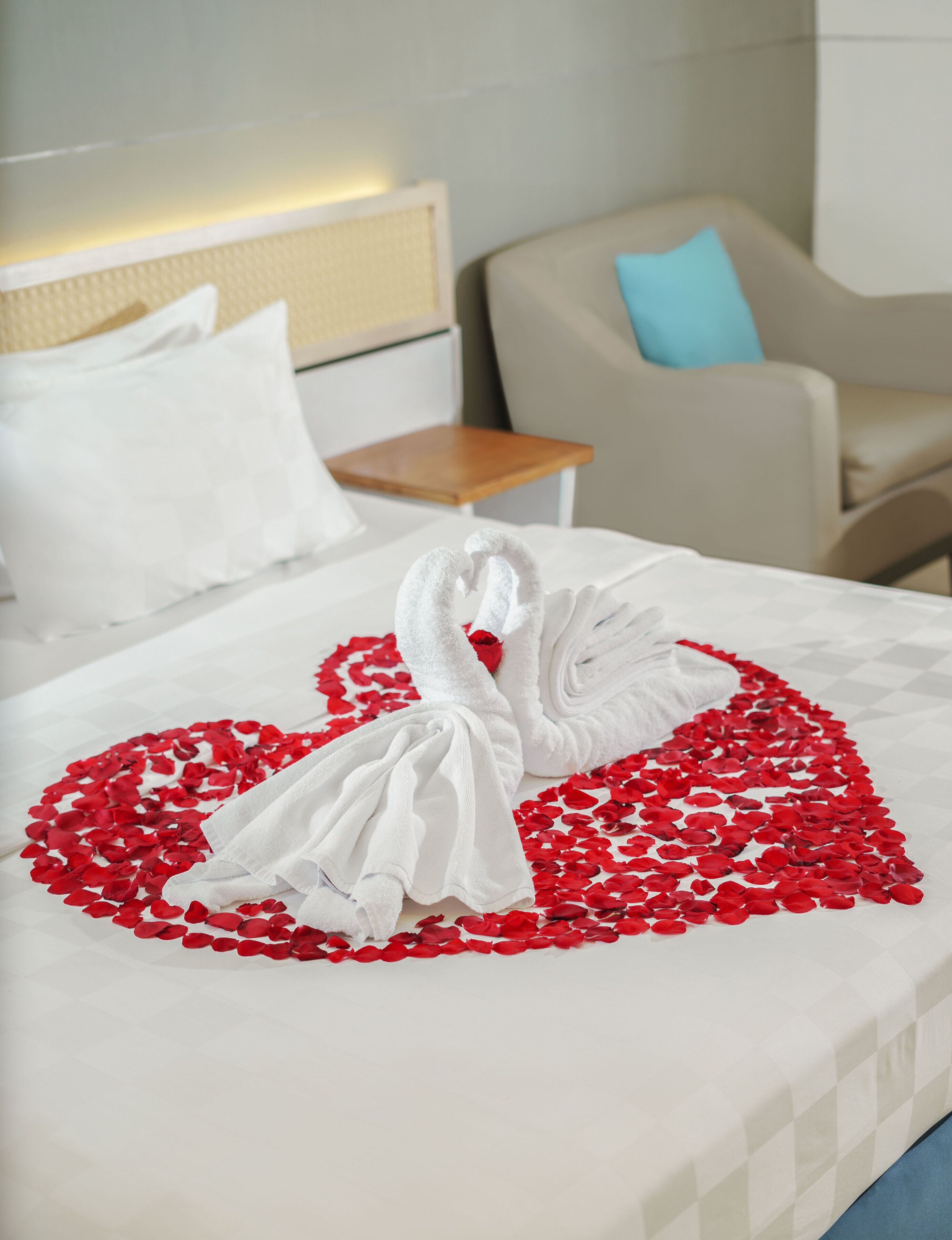 A bed with a heart-shaped towel arrangement and rose petals.