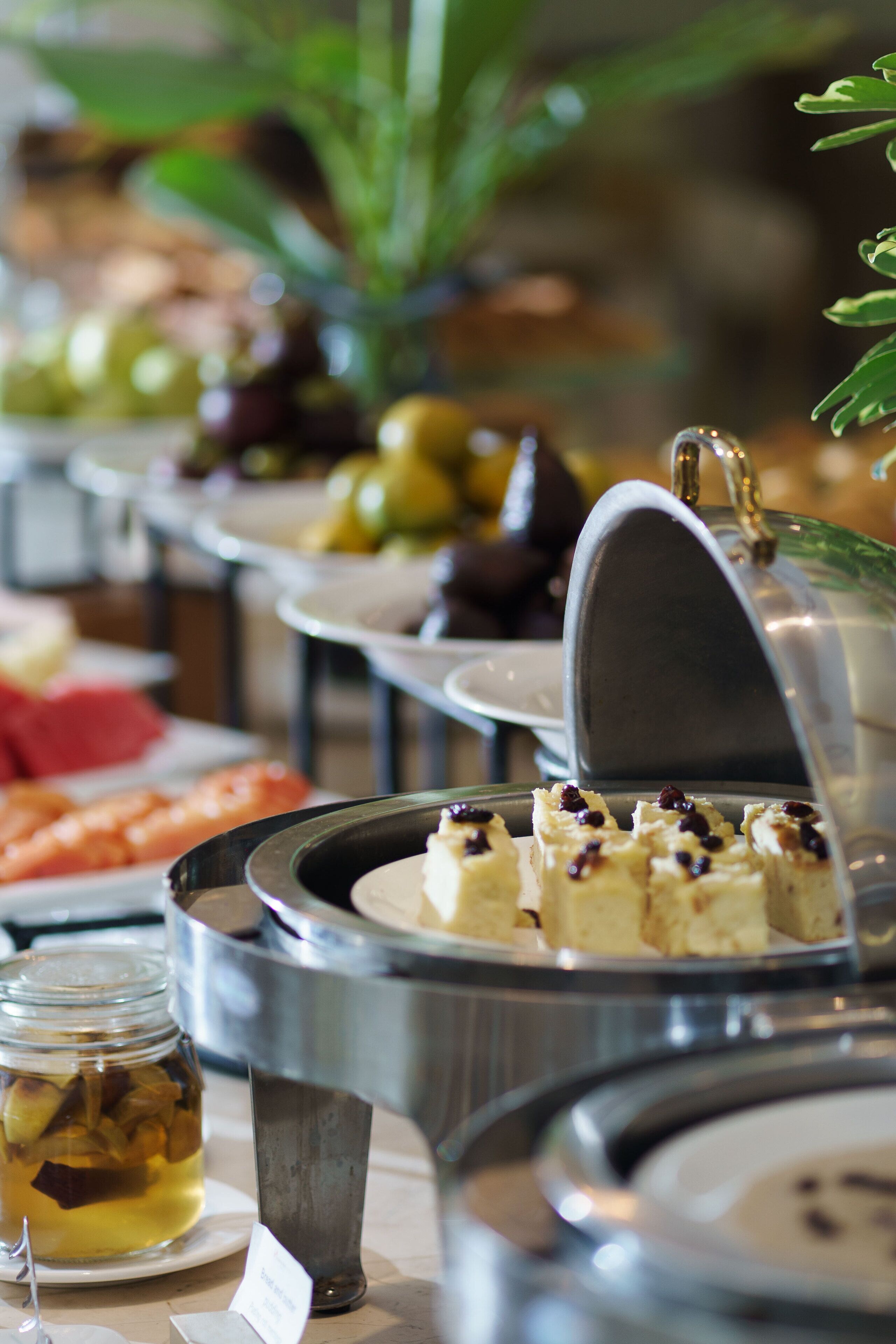 A buffet with various food items, including a jar of pickles and a dish with cubes of food topped with a dark ingredient.