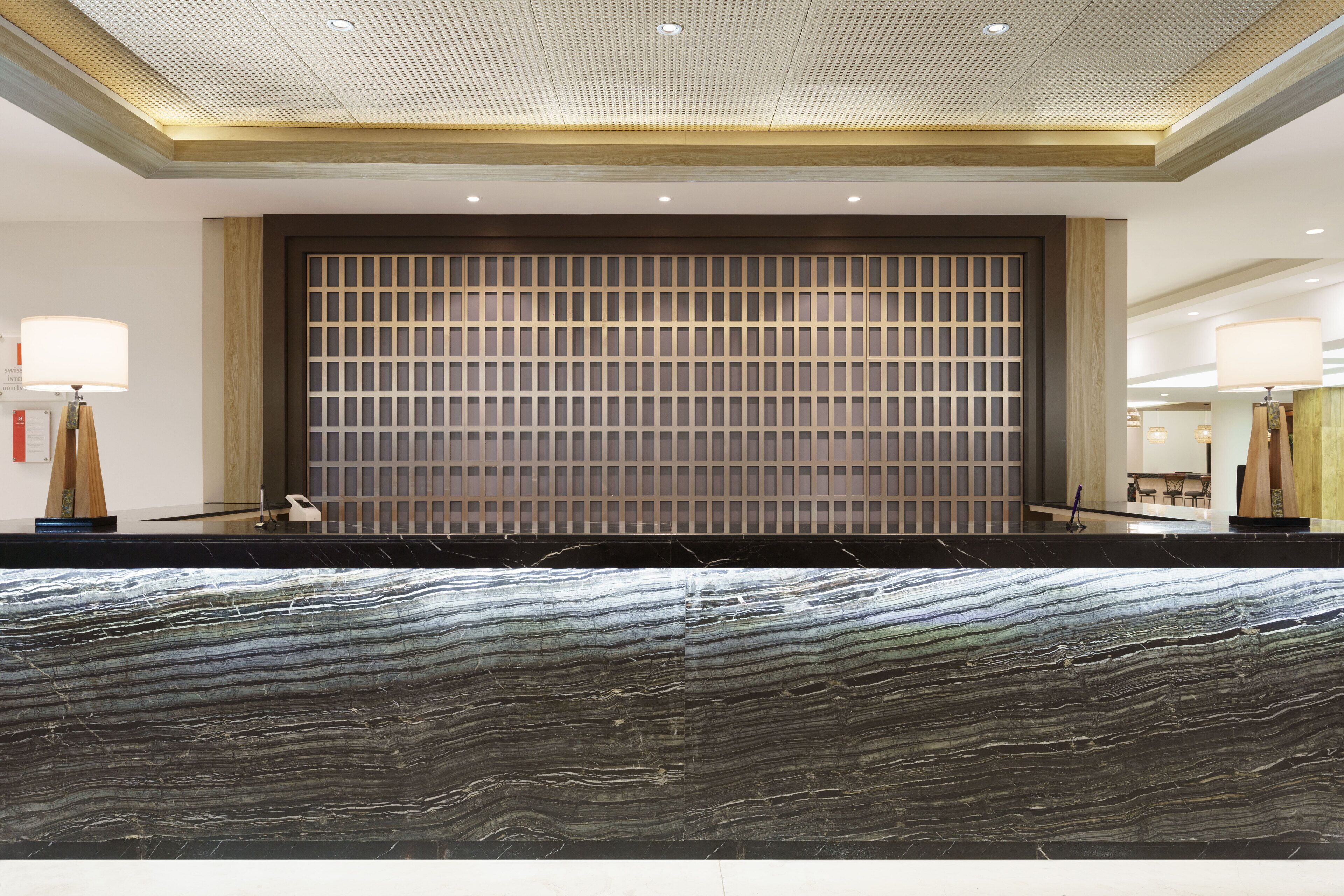 A reception area with a marble reception desk, a wooden panel wall, and a ceiling with recessed lighting.