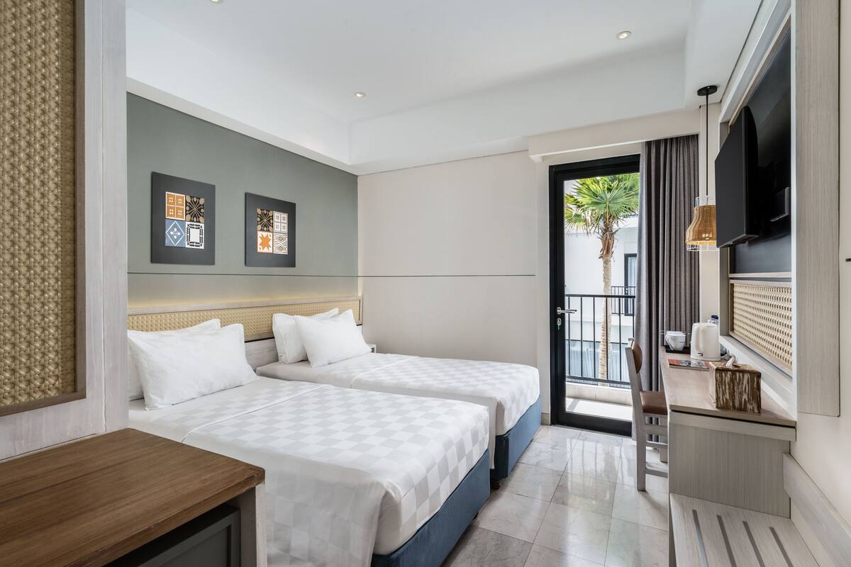A hotel room with two beds, a desk, a TV, and artwork on the wall.