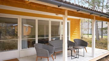 Un área de estar al aire libre techada con sillas de mimbre y una mesa, una terraza de madera y un ventanal que da a un porche cubierto.