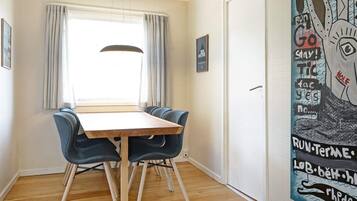 Un comedor con una mesa de madera y sillas azules, una ventana con cortinas y una pared con un cuadro abstracto grande.