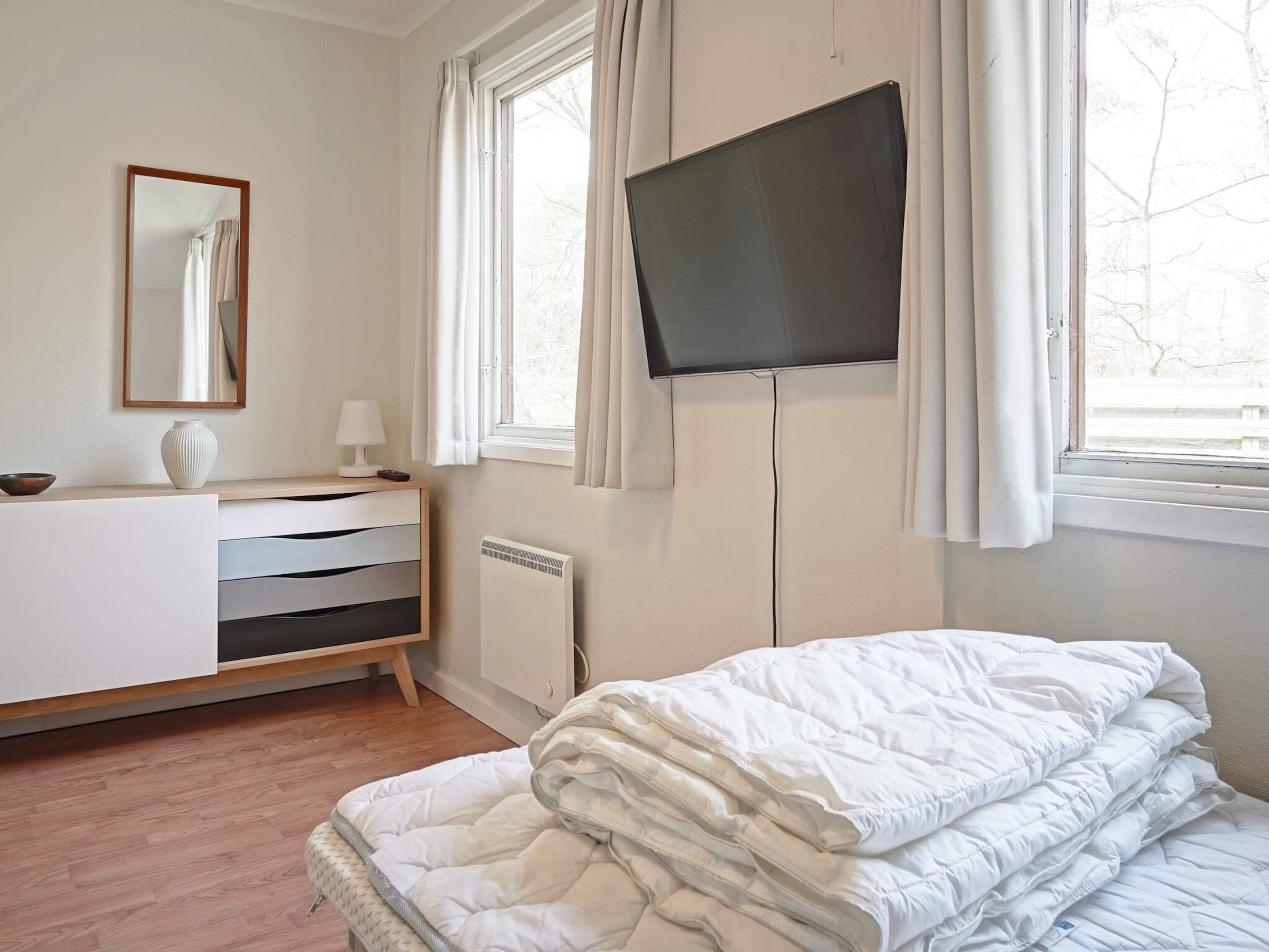 A bedroom with a bed, a dresser, a mirror, a television, and a window.