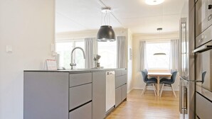 A modern kitchen with grey cabinets, a wooden dining table with chairs, and a large window with curtains. - 7 Person Holiday Home in Nexo (Nexø)