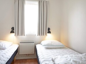 Una habitación con dos camas, una ventana con cortinas, un calentador de pared y dos lámparas de pared.