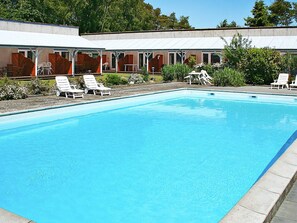 En pool med hvide liggestole og et overdækket siddeområde med røde puder.