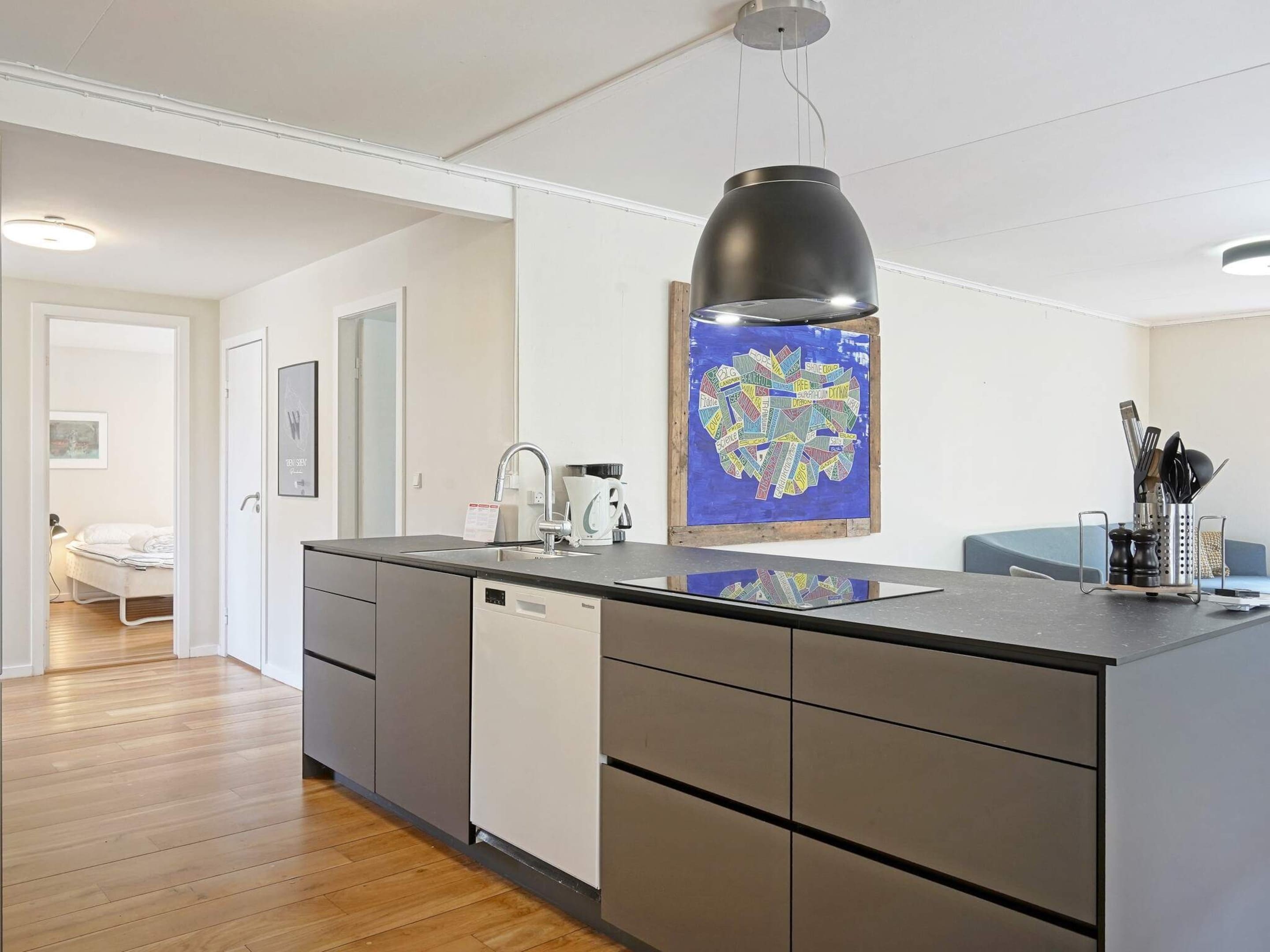A modern kitchen with a central island, a pendant light, and a colorful artwork on the wall.