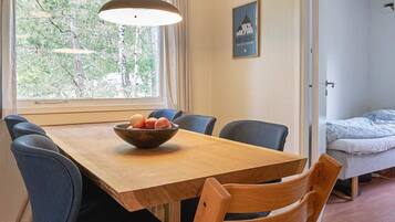 A dining area with a wooden table, blue chairs, a bowl of fruit, and a hanging light fixture.