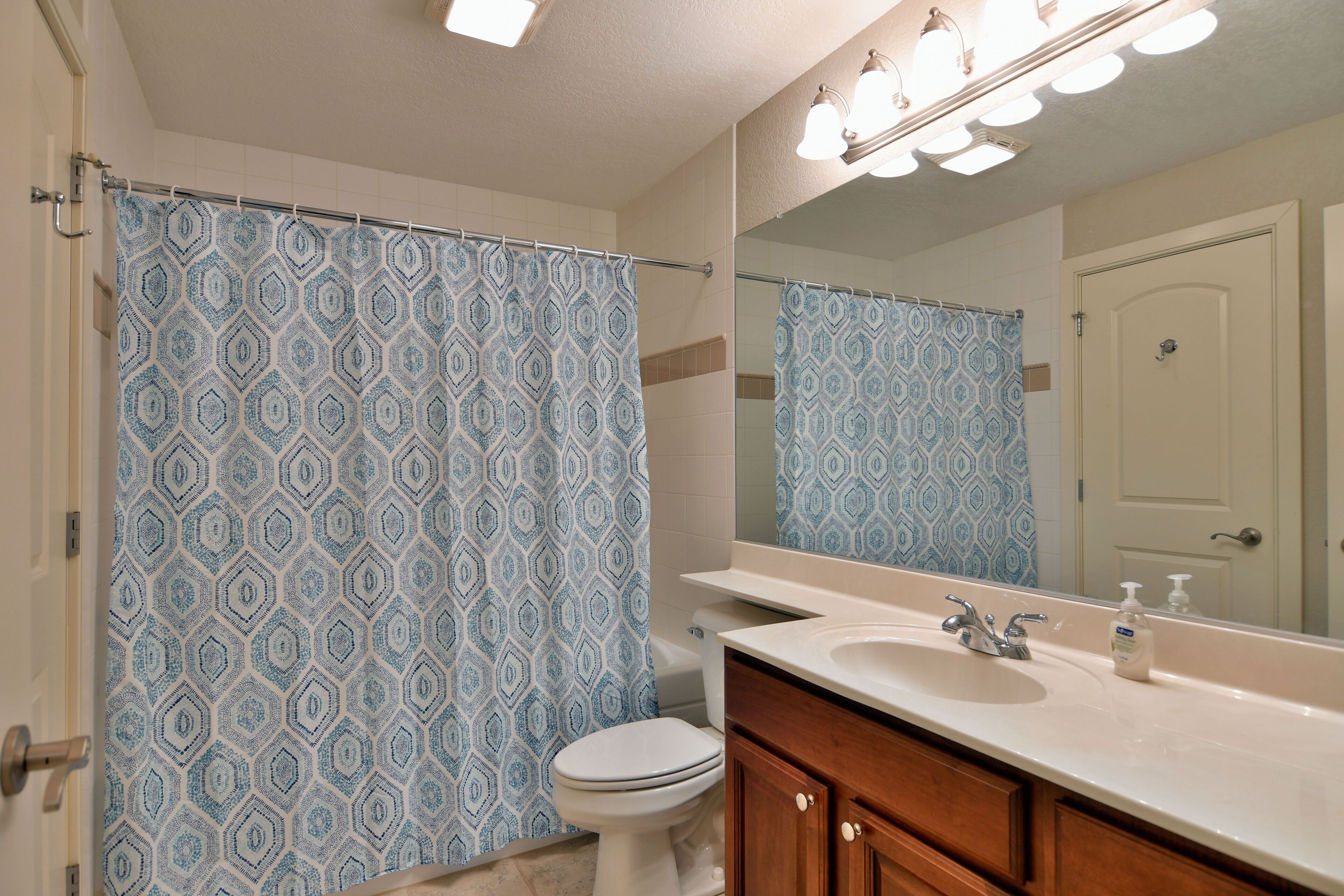 A bathroom with a patterned shower curtain, a toilet, a sink with a mirror, and wooden cabinets.