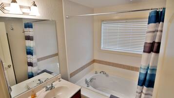 Une salle de bain avec un double lavabo, une baignoire, une fenêtre avec des stores et un rideau de douche.