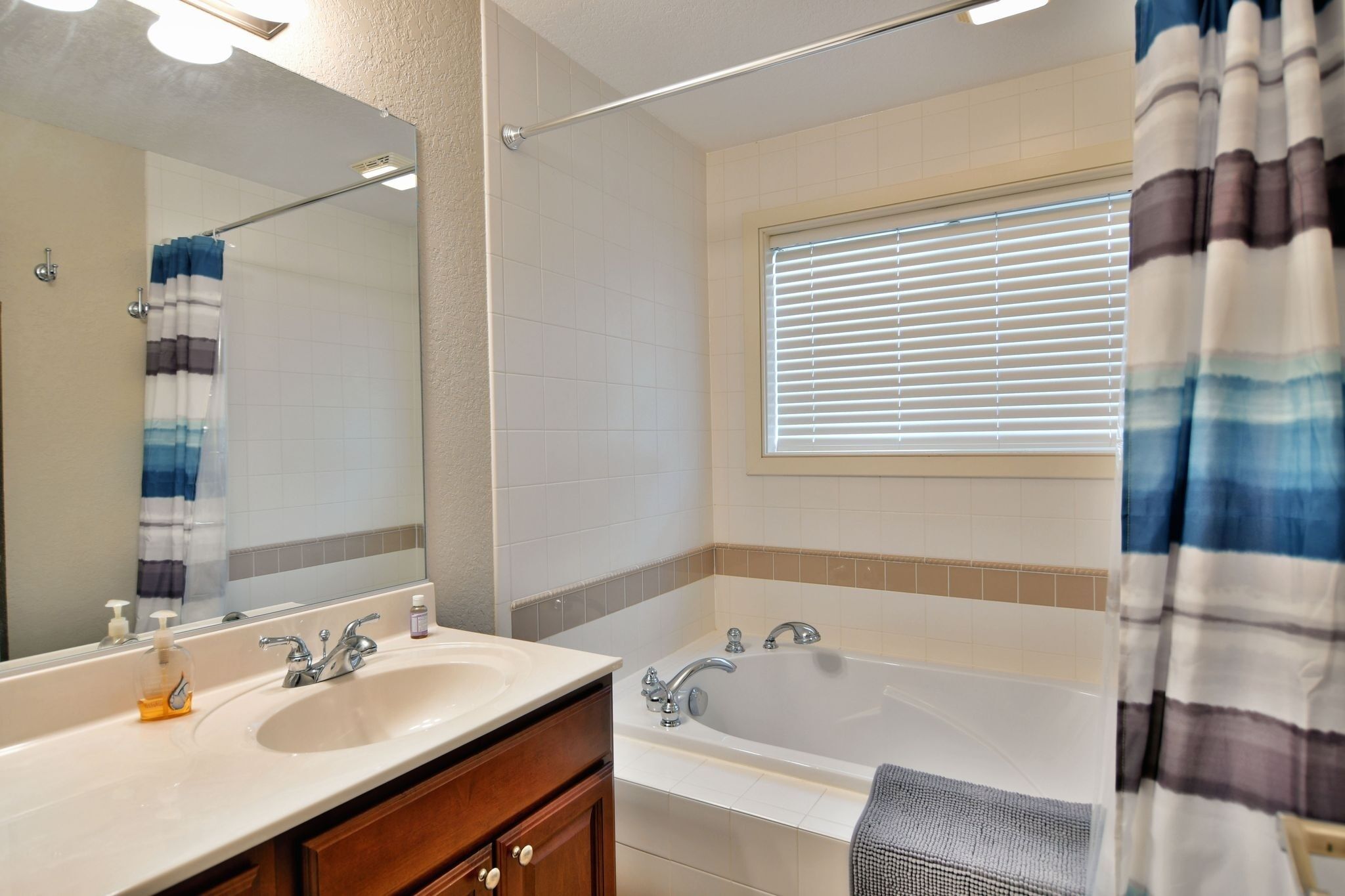 A bathroom with a bathtub, a sink, a mirror, and a window with blinds.