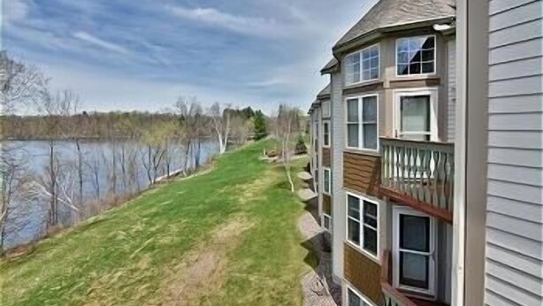Un edificio residencial de varios pisos con balcón, jardín con césped y vista al lago.