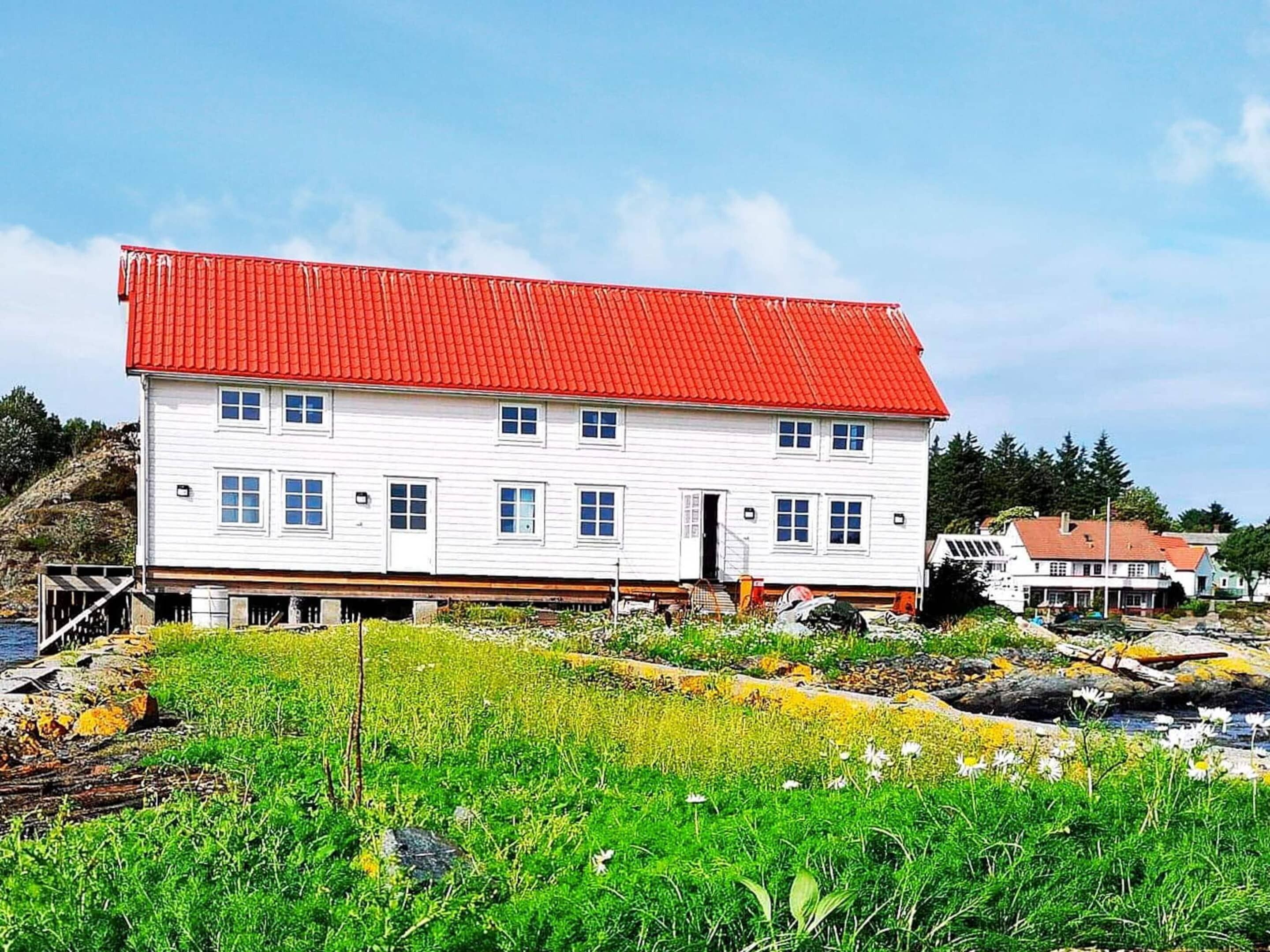 Un bâtiment blanc avec un toit rouge, situé au bord d’une étendue d’eau, avec une végétation verdoyante au premier plan.