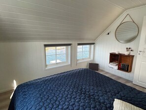 A bedroom with a large bed, two windows, a wooden shelf with books, and a mirror on the wall. - 12 Person Holiday Home in Bremnes-by Traum (Bomlo)