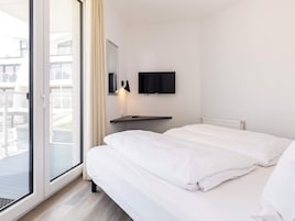 Una habitación de hotel con una cama, un televisor en la pared y un ventanal con cortinas.