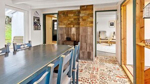 A dining area with a long table, blue chairs, a stone fireplace, and patterned flooring.