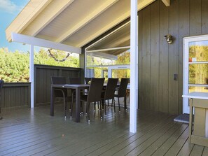 An outdoor patio with a wooden deck, a table with chairs, and a covered area with a view of trees.