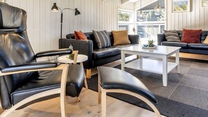 A modern living room with a black leather sofa, a black leather armchair, and a white coffee table. There are two black floor lamps and a large window providing natural light. - 6 Person Holiday Home in Hals-by Traum (Hals)