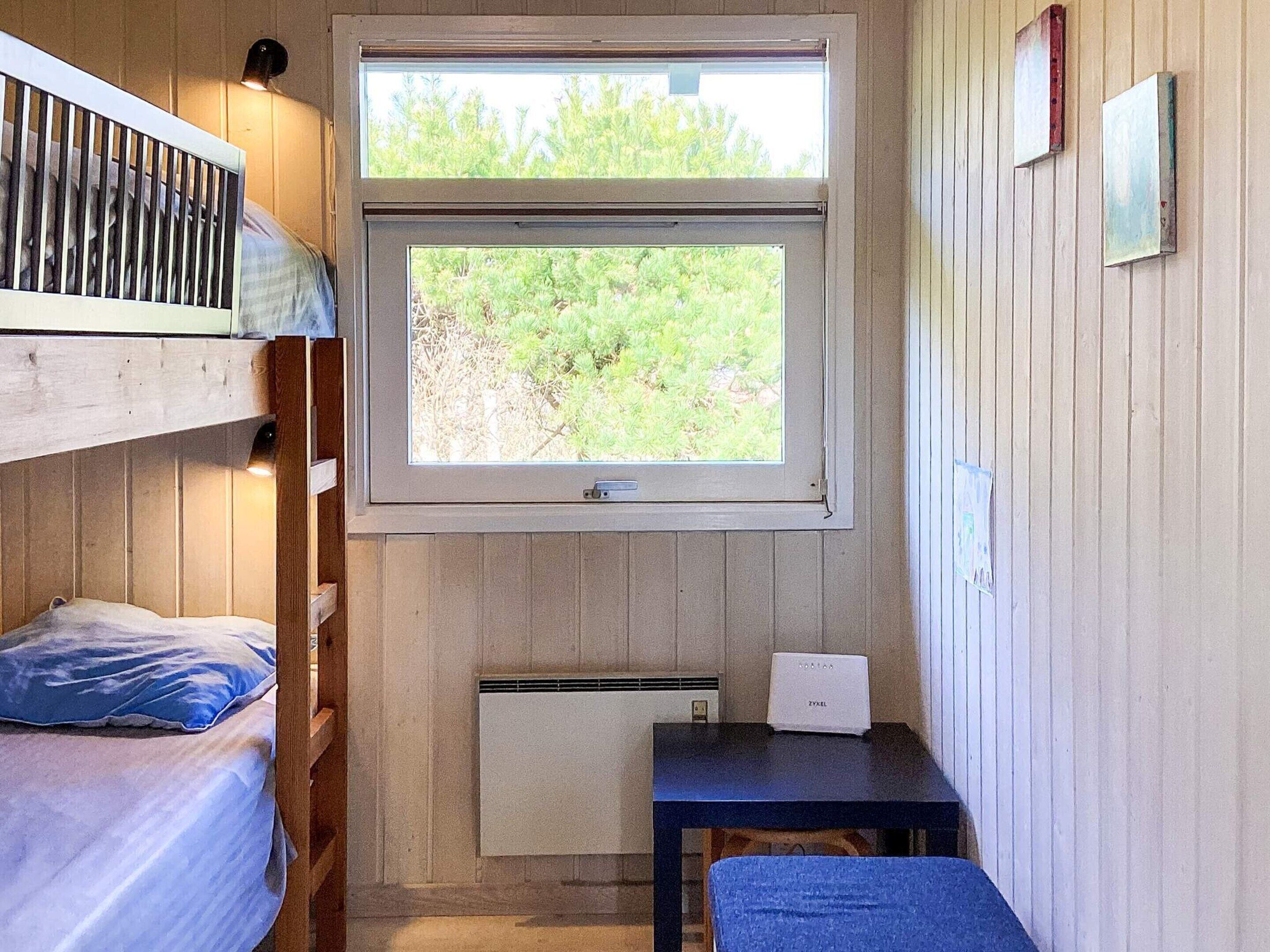 A small, cozy room with a bunk bed, a desk with a computer, and a window overlooking greenery.