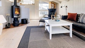 A cozy living room with a wood-burning stove, a black leather sofa, a white coffee table, and a black and white patterned rug. - 6 Person Holiday Home in Hals-by Traum (Hals)
