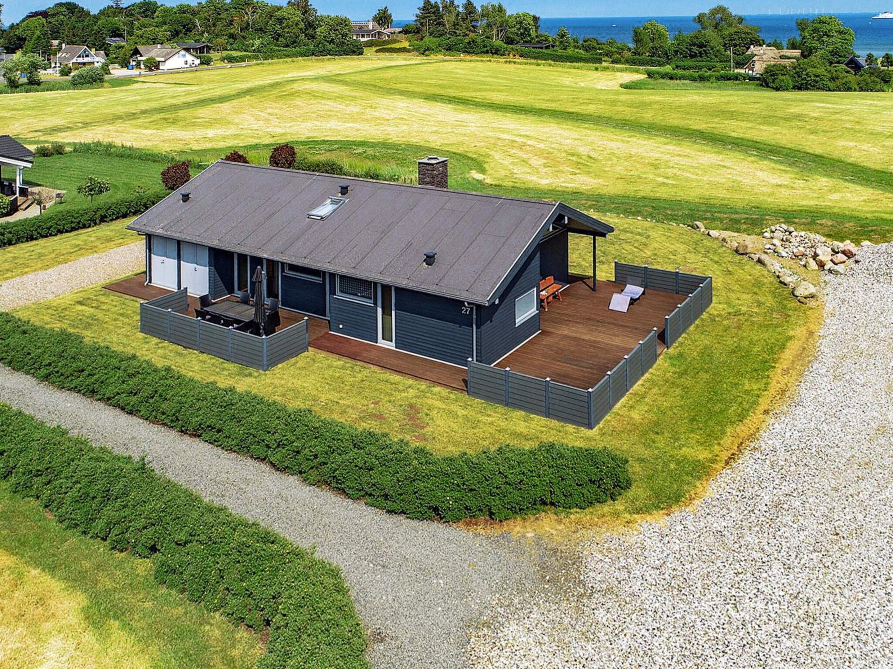 A modern house with a deck, large windows, and a view of the ocean.