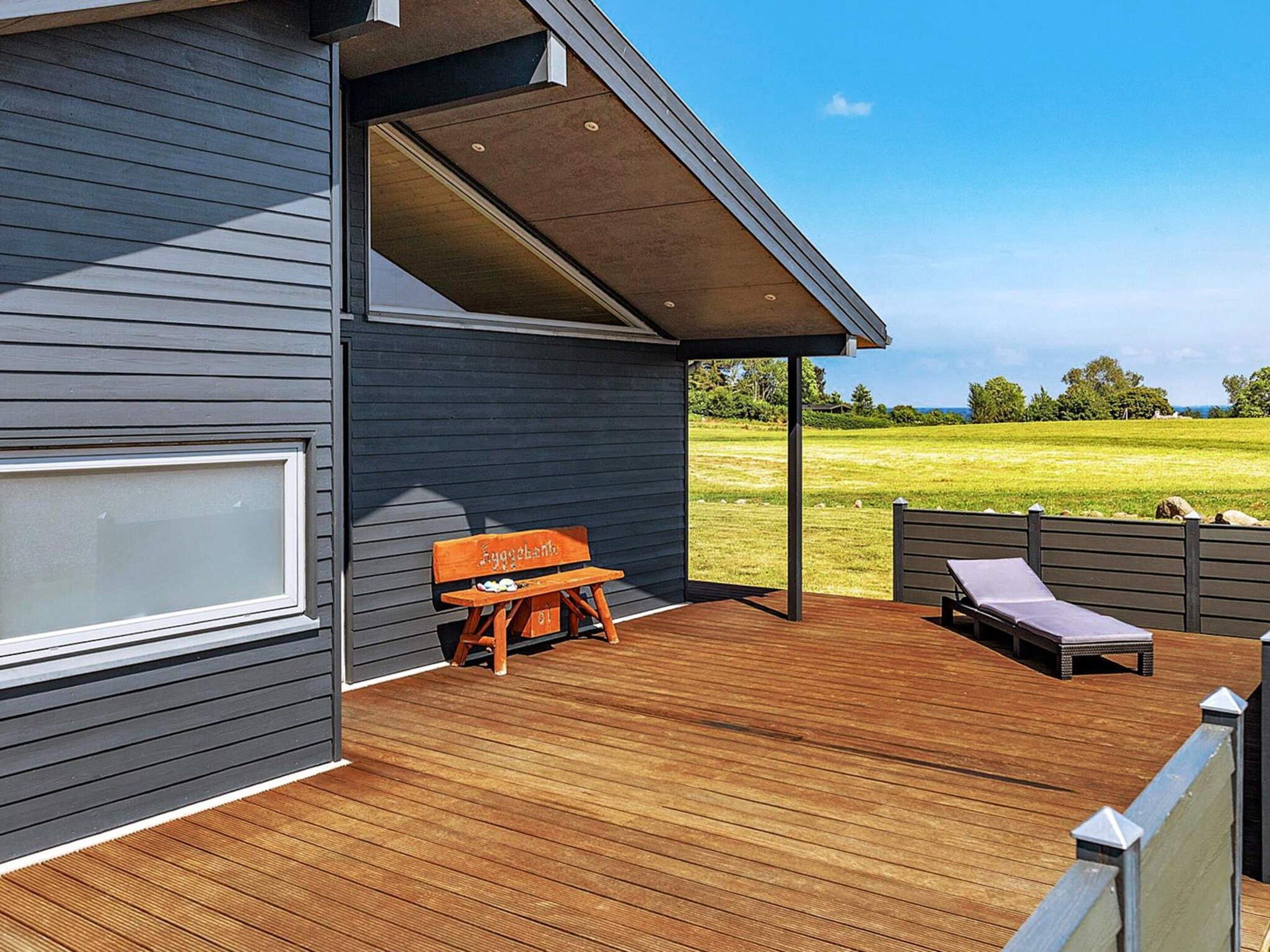 A modern house with a wooden deck, a bench, and a lounge chair.