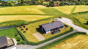 Une vue aérienne d’une propriété rurale avec une grande maison, de vastes champs et une étendue d’eau en arrière-plan.