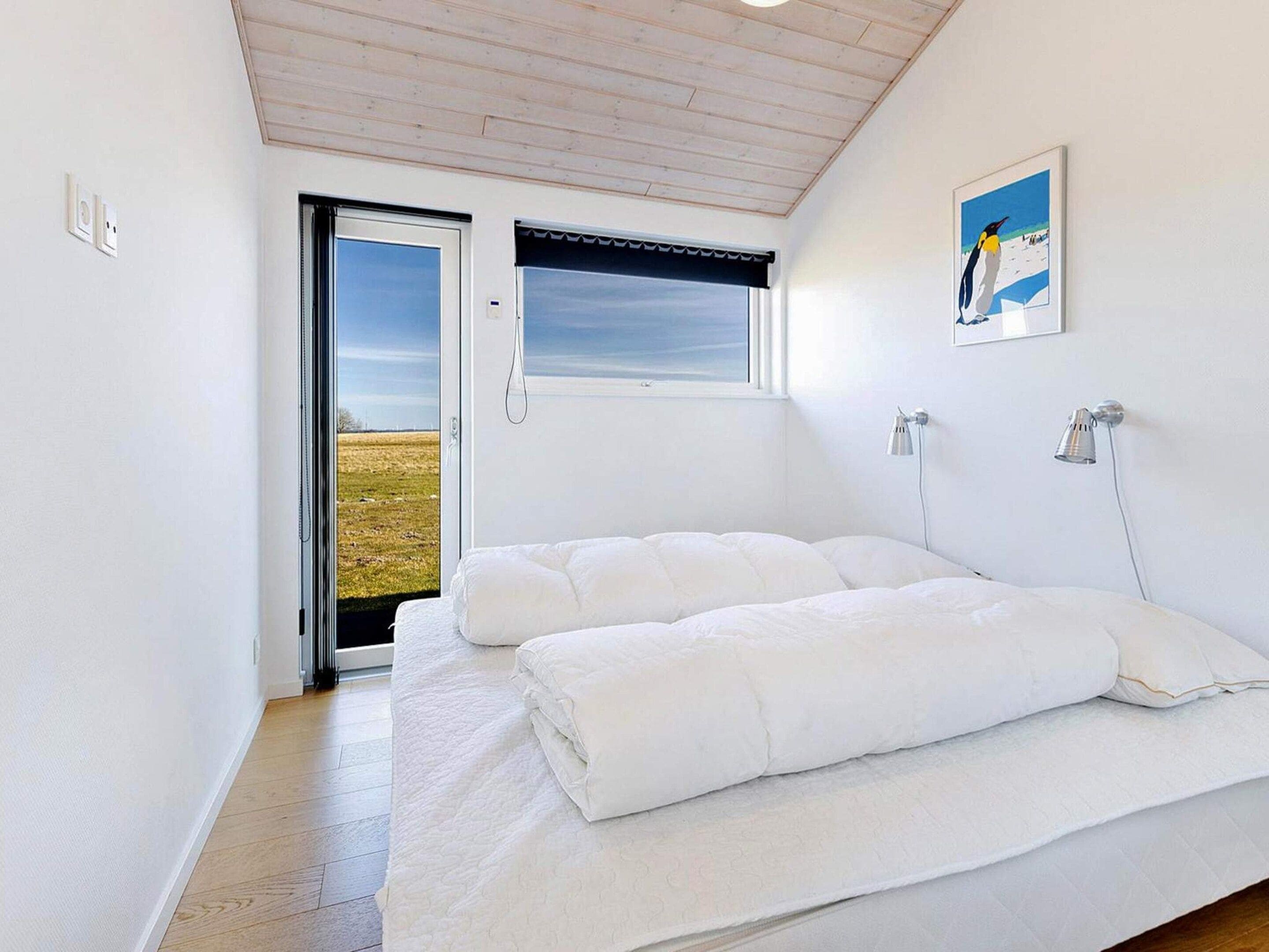 A bedroom with a bed, a window with a view, a painting, and a door leading outside.