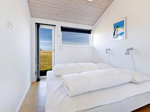 A bedroom with a bed, a window with a view, a painting, and a door leading outside.