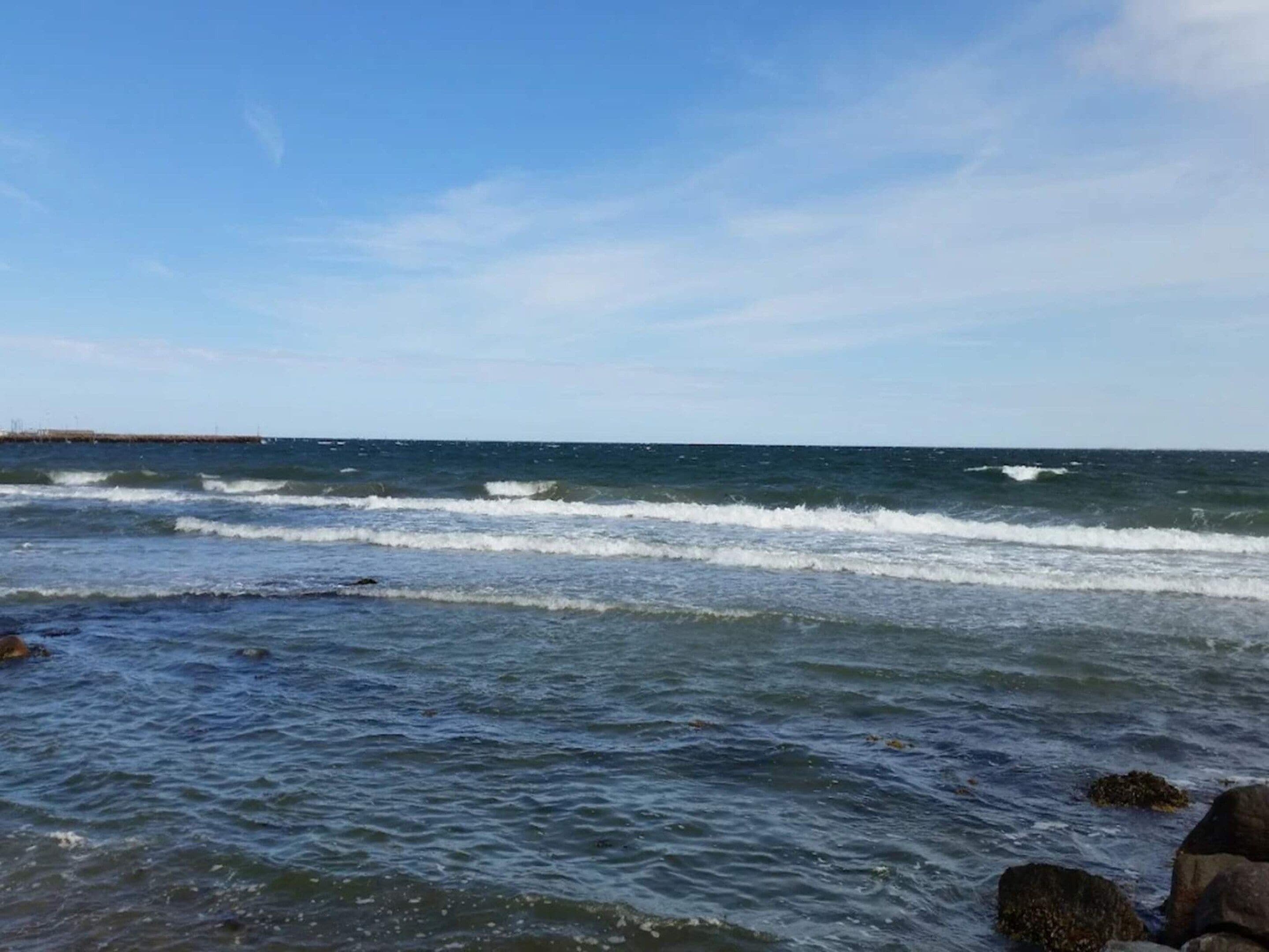 Une vue sur la côte, avec des vagues, des rochers et un ciel dégagé.