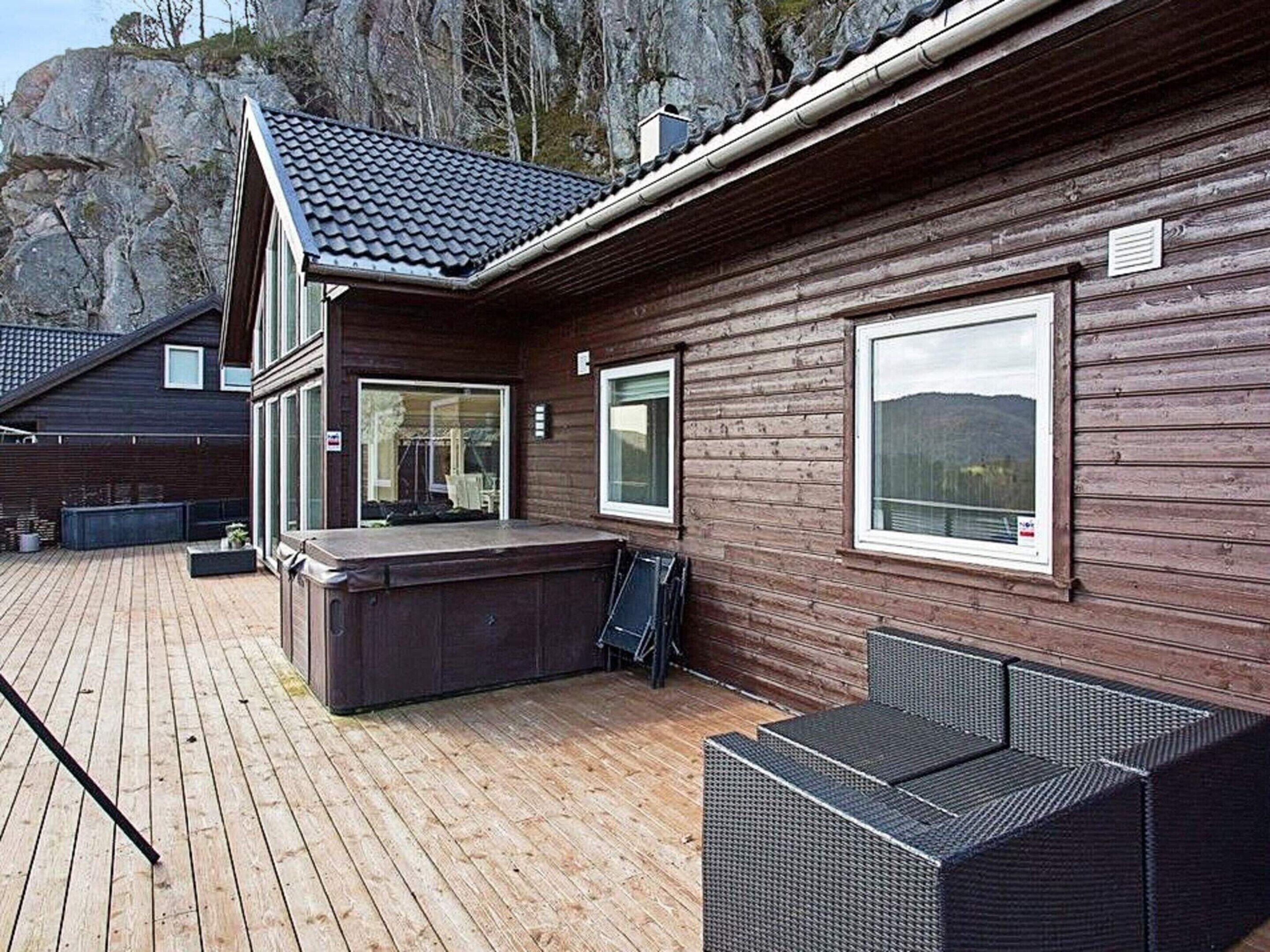 A wooden cabin with a deck, large windows, and a hot tub.